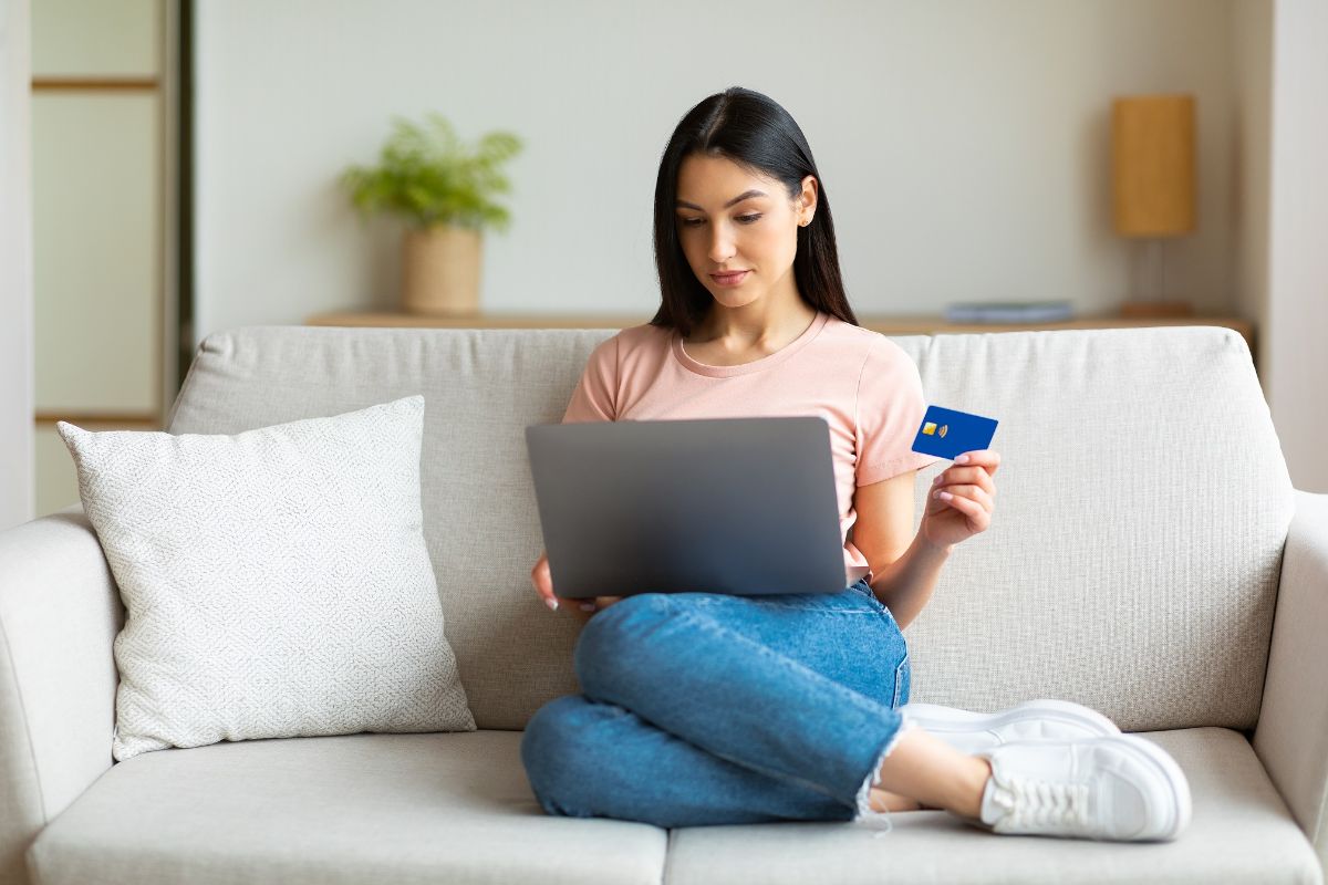 Femme faisant des achats en ligne à l'aide d'un ordinateur portable et d'une carte de crédit assis sur un canapé à la maison pendant le week-end